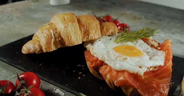 Сэндвич с круассаном со сливочным сыром, лососем и яйцом на черной тарелке — стоковое видео