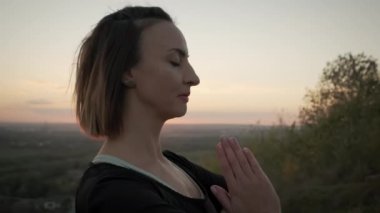 Portre Kadını yoga minderinde duruyor ve gün batımında dışarıda yoga esneme egzersizi yapıyor.