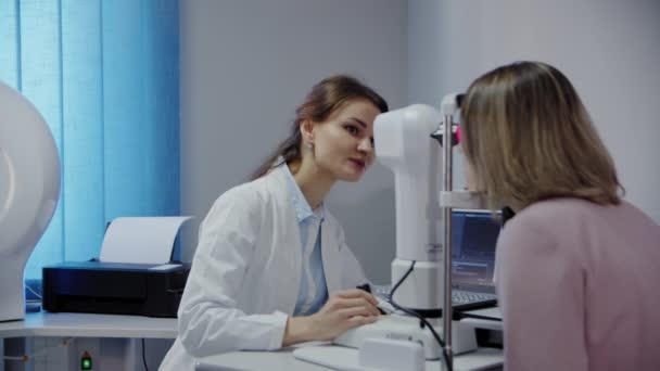 Офтальмолог осматривает глаза пациентов, а затем смотрит в камеру. Широкий обзор — стоковое видео