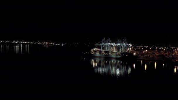 Široký záběr nákladní lodi s nákladními kontejnery stojí na kotvišti v přístavu při nakládce a vykládce kontejnerů v noci — Stock video