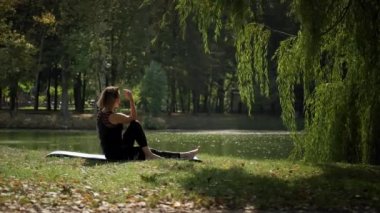 Yoga minderinde oturan ve güneşli bir günde dışarıda yoga esneme egzersizi yapan bir kadın. Geniş görüntü