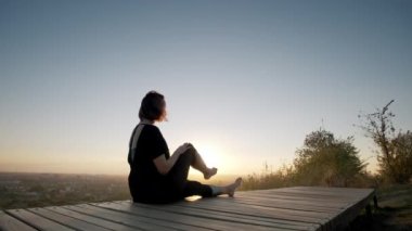 Yoga minderinde bir kadın ve gün batımında dışarıda yoga egzersizi yapıyor. Geniş görünüm