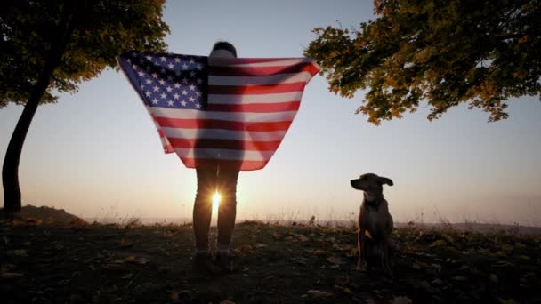 Achteraanzicht van een vrolijke vrouw met USA nationale vlag die bij zonsondergang buiten staat. Breed schot — Stockvideo