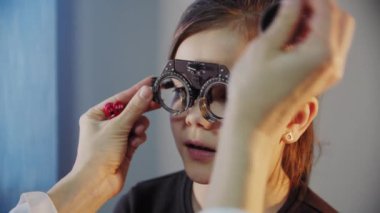 Kapatın. Göz doktoru genç kızın gözünü muayene eder ve gözlük için lens seçen bir cihaz takar.