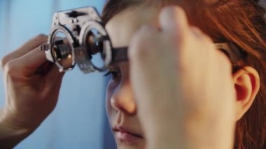 Manzarayı kapat. Göz doktoru genç kızın gözünü muayene eder ve gözlük için lens seçen bir cihaz takar.