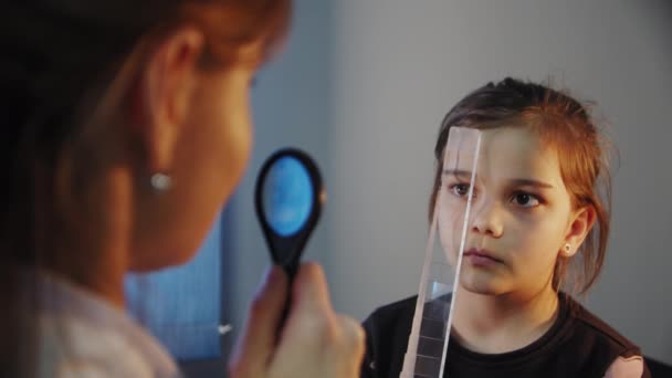 Κοίτα από κοντά. Ο οφθαλμίατρος εξετάζει την ασθενή έφηβος μάτι κορίτσι και βάζει σε μια συσκευή για την επιλογή φακών για τα γυαλιά — Αρχείο Βίντεο