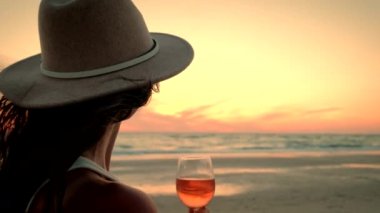 Şarabı elinde tutan kadın okyanusun üzerinde gün batımını seyrediyor ve harika manzaranın tadını çıkarıyor. Yavaş çekim