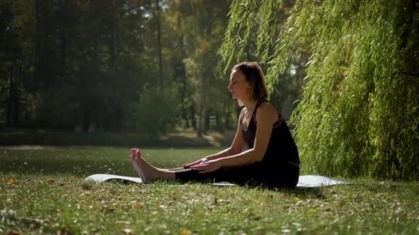 Donna seduta su tappetino yoga e praticare esercizio di yoga all'aperto nella giornata di sole. Rallentatore — Video Stock