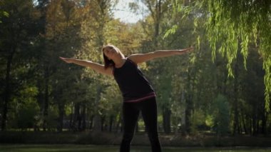 Yoga minderinin üzerinde duran ve güneşli bir günde dışarıda esneme egzersizi yapan kadın geniş görüşlü. Yavaş çekim görüntüleri