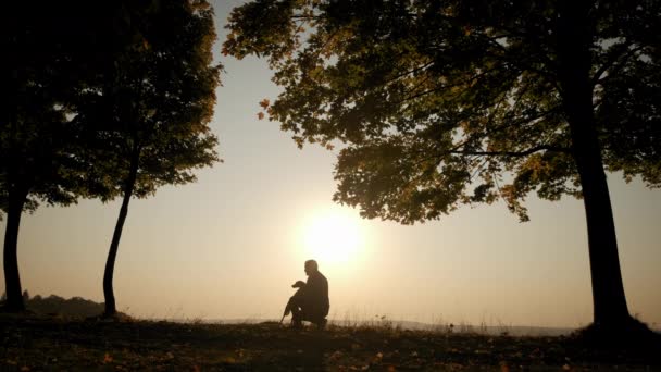 Sullo sfondo del cielo arancione del tramonto Silhouette di un uomo che cammina con un cane durante il tramonto stupefacente. Colpo al rallentatore — Video Stock