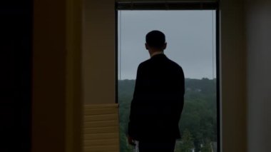 Siyah takım elbiseli bir işadamı binalara bakan büyük bir pencereye doğru yürüyor. Yavaş çekim.