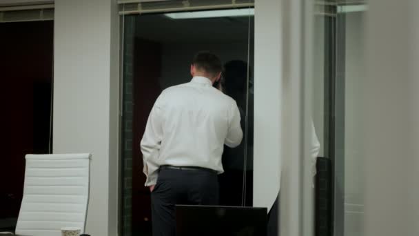 Businessman in black suit using smartphone, and looking out the window at skyscrapers at night — 图库视频影像