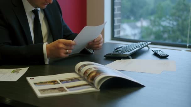 Empresario en traje negro sentado en una mesa y revisando documentos — Vídeos de Stock