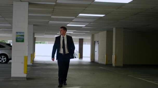 Empresario con traje negro camina por el aparcamiento. — Vídeos de Stock