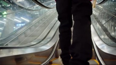 Kırmızı Noel kazaklı bir adam elinde kırmızı bir çantayla alışveriş merkezindeki yürüyen merdivene biniyor.. 