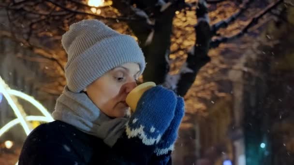 Щаслива усміхнена жінка п'є каву або чай вночі в Різдвяному місті над снігом падає — стокове відео