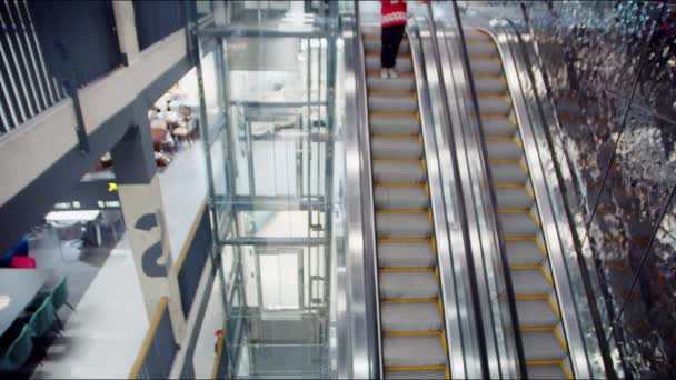 Un homme dans un pull de Noël rouge tient un cadeau dans ses mains et monte sur l'escalier roulant dans le centre commercial. Gros plan — Video