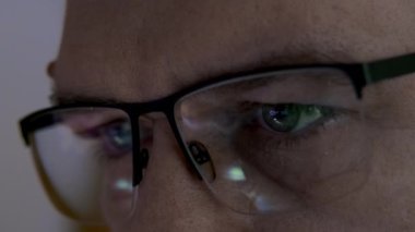 Manzarayı kapat. Gözlüklü Adam 'ın Gece Gözlüğü' nün yansıması, Yorgun İşadamı internet kullanıyor, internette geziniyor, hisse senetlerindeki iş dinamiklerini izliyor.