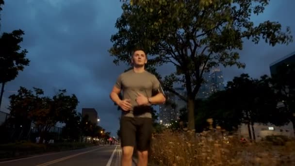 Jovem desportista do sexo masculino com corpo atlético está correndo com esforço e dedicação no centro da cidade. Vista frontal — Vídeo de Stock