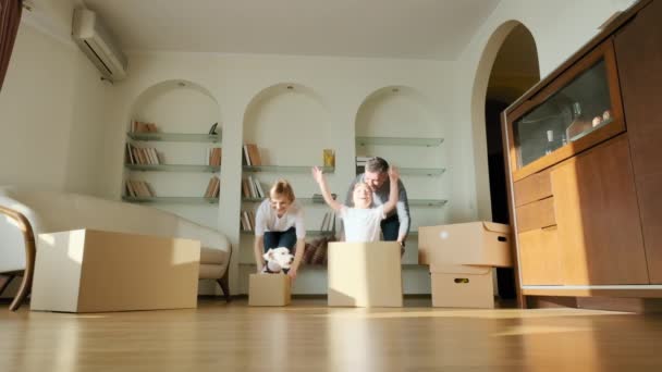 Excited happy young parents run push cardboard boxes ride insideand pets dog Jack Russel , family homeowners playing having fun on moving day. Slow view footage — Stock Video