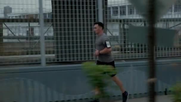 Young male sportsman with athletic body is running with effort and dedication in city center. Side view footage — Vídeos de Stock