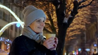 Mutlu, güler yüzlü bir kadın, Noel 'de kar yağarken ve telefon görüşünü kullanırken gece vakti hazır kahve içiyor.