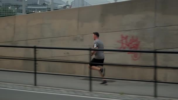 Atletik vücutlu genç erkek sporcu şehir merkezinde gayret ve adanmışlıkla koşuyor. Yan görüntü. Yavaş çekim. — Stok video