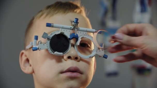 Close up view shot . The ophthalmologist examines the patient teen boy eye and puts on a device for selecting lenses for glasses — стоковое видео