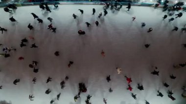 Aerial drone view of people skating on an outdoor skating rink in winter at night in City, with dark nighttime lighting. 