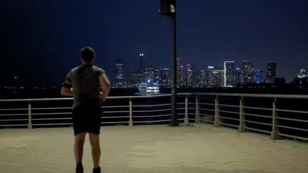 Side view of Young male sportsman with athletic body is running with effort and dedication in city center. Wide view — Video Stock