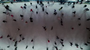 Aerial drone view of people skating on an outdoor skating rink in winter at night in City, with dark nighttime lighting. Top view