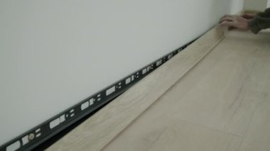 Installation of plastic floor plinth. Close up view of Worker mounts a plastic plinth on the parquet floor