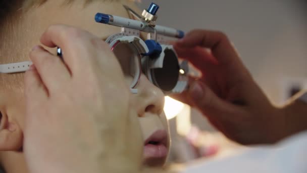 Close up footage of ophthalmologist examines the patient teen boy eye and puts on a device for selecting lenses for glasses — 비디오