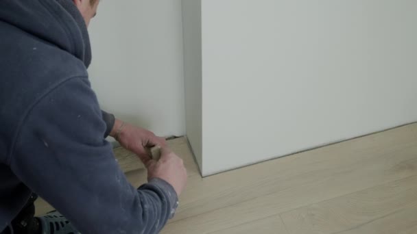 Installation of plastic floor plinth. Close up shot of Worker mounts a plastic plinth on the parquet floor — Stockvideo