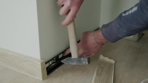 Installation of plastic floor plinth. Close up shot of Worker mounts a plastic plinth on the parquet floor — Wideo stockowe