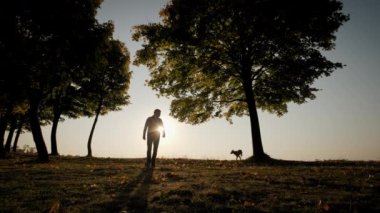 Wide shot. Against the background of the bright orange sunset sky Silhouettes of a man with a dog during amazing sunset. Slow motion shot
