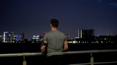 Young male sportsman with athletic body is running on the pier near the sailing ship at night. Back view
