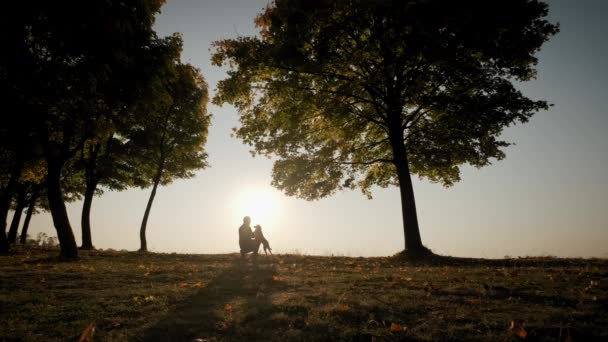 Brede opname beelden. Tegen de achtergrond van de feloranje zonsondergang hemel Silhouetten van een man met een hond tijdens een geweldige zonsondergang. Slow motion shot — Stockvideo