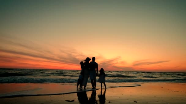 Silhouetted happy family stand on the beach at sunset. — Stock Video