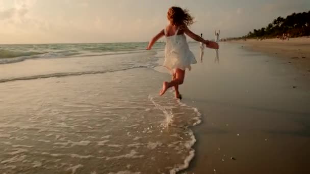 Mała dziewczynka w białej sukience biegnie wzdłuż plaży do ojca. — Wideo stockowe
