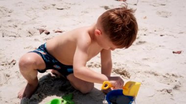 Küçük çocuk kumsalda kumla oynuyor okyanusta ve kumdan kale evi inşa ediyor..