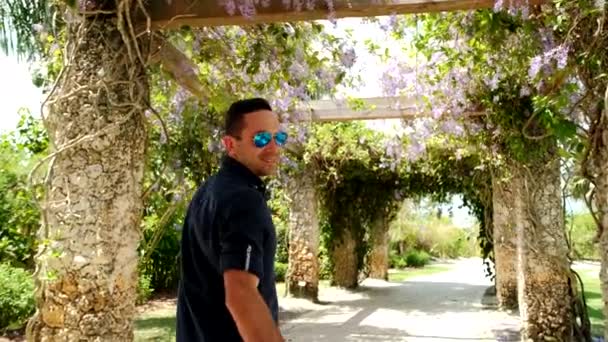 Wide view footage of Young couple man and woman in red dress walks through the garden and turns around, smiling. Slow motion. — Stock Video