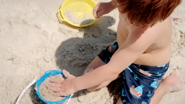 Mały chłopiec bawiący się piaskiem na plaży ocean morze i budowa piasku zamek dom. Widok z góry — Wideo stockowe