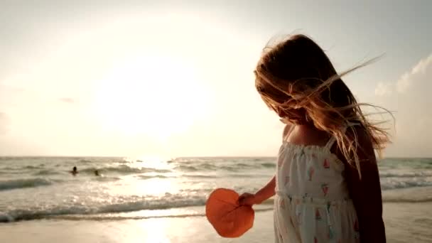 Een klein meisje in een witte jurk loopt langs het strand — Stockvideo