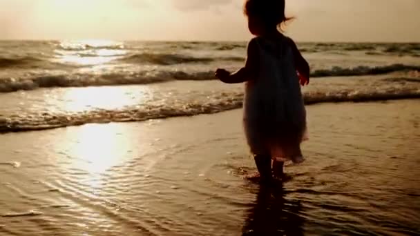 Een klein meisje in een witte jurk staat langs het strand — Stockvideo