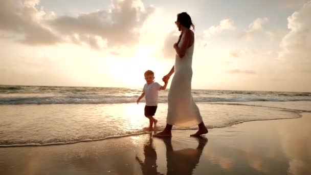 Moeder en zoon lopen samen op het strand bij zonsondergang — Stockvideo