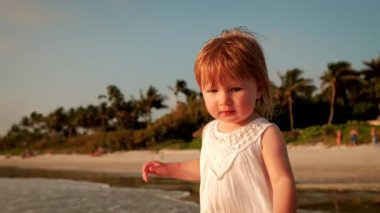 Sahilde beyaz elbiseli küçük bir kız duruyor. Kapat.