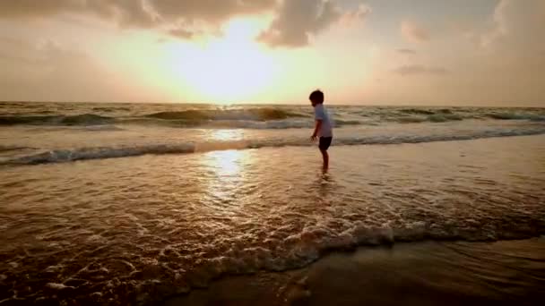Chico feliz corriendo en la playa al atardecer. Movimiento lento — Vídeos de Stock