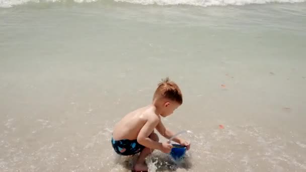 Mały chłopiec bawiący się piaskiem na plaży ocean morze i budowa piasku zamek dom. Nagranie z wolnego ruchu — Wideo stockowe