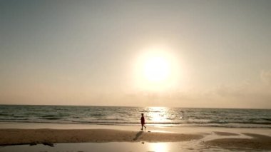 Gün batımında güzel bir sahilde yürüyen bir kadının silüeti..